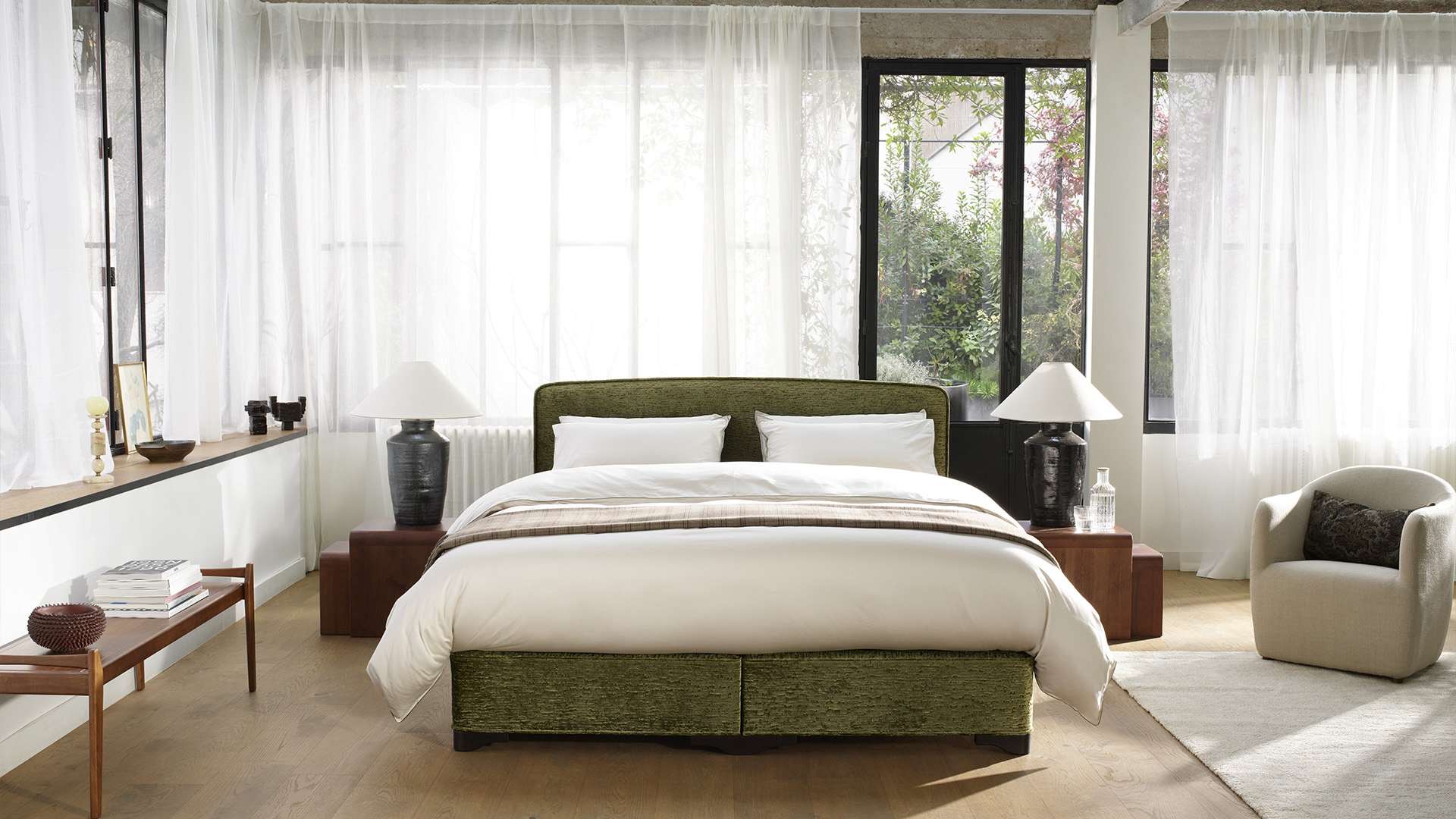 Vispring Classic Bett mit olivgrünem Samtbezug in einem hellen Loft mit Gartenblick